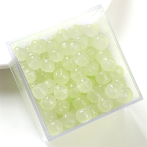 Close-up of pale yellow translucent glass beads in a transparent plastic container