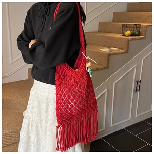Close-up of red handmade woven cotton tote bag with stylish fringe tassels on stairs