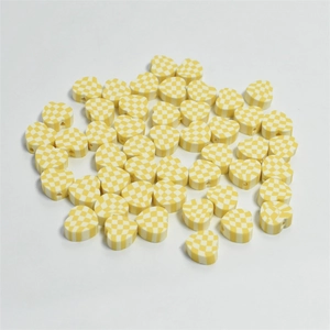 Detailed view of yellow and white checkered heart clay beads for DIY jewelry making