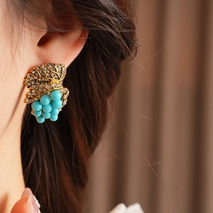 Macro shot of vintage grape cluster stud earrings with gold leaves and turquoise beads