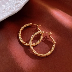 Detail der goldenen Creolen mit gehämmertem Metall auf luxuriösem rotem Seidenhintergrund