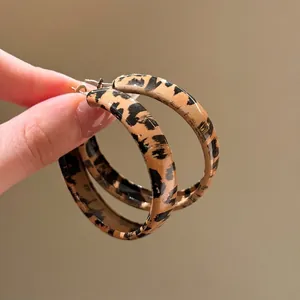 Orecchini a cerchio in resina con stampa leopardata marrone e nera tenuti in mano con cura