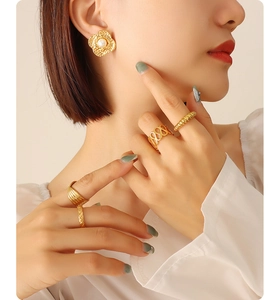 Close-up of pearl flower earrings and golden textured rings worn by a model