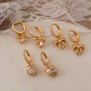 Set of three 18K gold plated bow and heart zircon drop earrings on a lace background