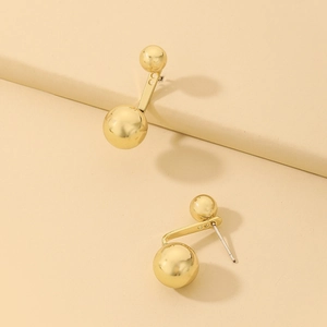 Detailed close-up of golden dual-sphere metal earrings on a minimalist geometric stand