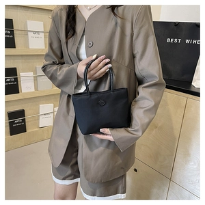 Sac seau chic en nylon noir avec logo, tenu par un mannequin en tailleur marron élégant
