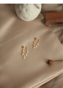 Detailed view of elegant gold tassel earrings with white pearls on a silk background