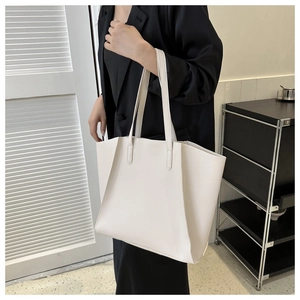 Detail view of a large white faux leather tote bag worn by a model in professional attire