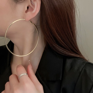 Close-up of large minimalist gold hoop earrings and silver ring on elegant model