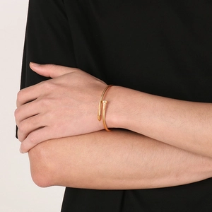Detailed view of a gold nail-shaped twisted steel wire bracelet worn by a model