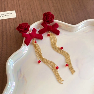 Macro detail of vintage red velvet flower earrings with golden tassel and bead accents
