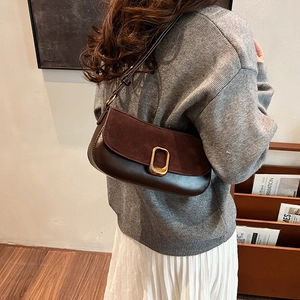 Brown textured underarm bag with gold geometric buckle worn over a grey sweater