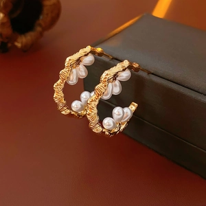 Detailed view of C-shape gold earrings with wrinkled texture and white teardrop pearls