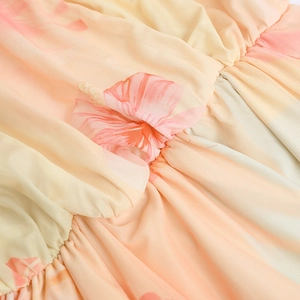Close-up of pink hibiscus print on ruched mesh fabric with a soft orange gradient