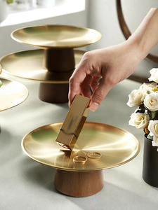 Detail showing hand placing item on a gold metal tray with wooden base and rings