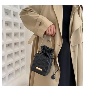 Detail of black quilted bucket bag with gold chain strap on a khaki coat outfit