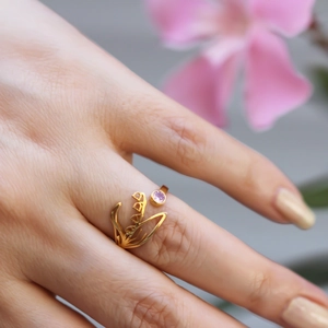 Close-up of gold flower ring with pink gemstone on model featuring elegant floral details