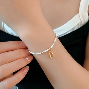 Macro view of bohemian style white seed bead bracelet with golden conch shell charm detail