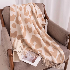 Chic cow print faux cashmere scarf with tassels draped on a warm brown wooden chair