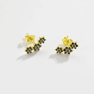 Close-up of elegant gold flower stud earrings with black zircon stones on white background