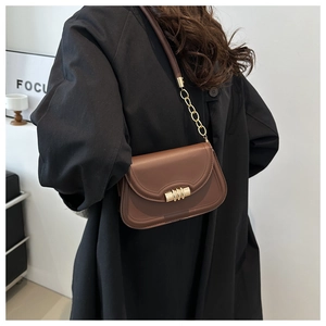 Detailed side view of a brown saddle bag featuring gold cylindrical clasp and chain strap