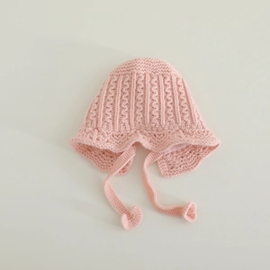 Detail of pink knitted baby hat featuring lace texture, chin straps and soft lining