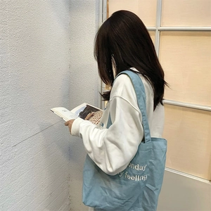 Detail of light blue denim tote bag featuring white embroidered letters and minimalist style
