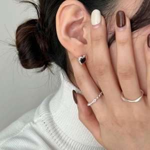 Close-up of minimalist black heart stud earrings and thin silver ring on a model