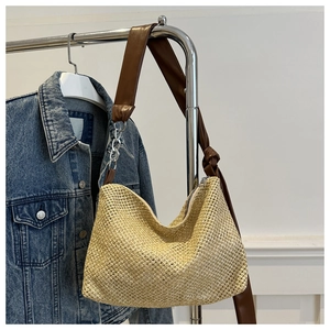 Detail of woven straw tote bag with brown leather and silver chain strap on denim