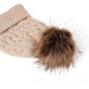 Detail of light beige cable knit winter hat featuring a large dark brown faux fur pom-pom