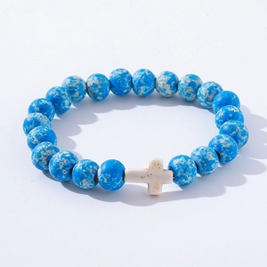 Detail view of blue turquoise stone beads bracelet with a white cross charm on a white background