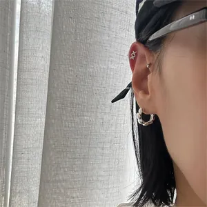 Detailed view of silver star stud earrings and thick wavy hoop on model's ear