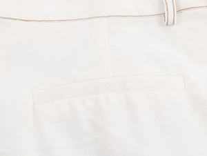 Detailed close-up of contrast brown stitching on white high-waisted wide-leg trousers