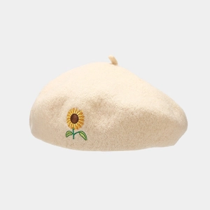 Close-up of golden sunflower embroidery on a beige wool beret hat with detailed texture