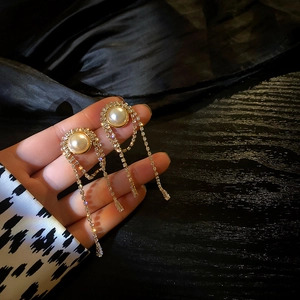 Macro detail of gold tassel earrings with pearls and crystals held on black satin background