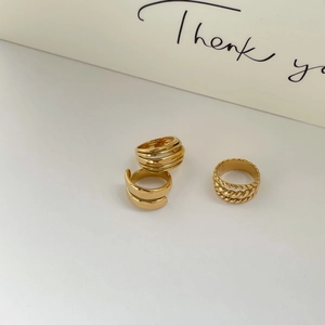 Detailed view of three minimalist gold multilayer rings and a woven twist band on white surface