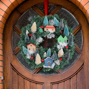 Light-up Christmas wreath with colorful miniature houses and pine needles on a wooden door