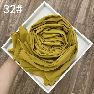 Détail d'une écharpe en mousseline jaune moutarde avec paillettes dorées et plis élégants