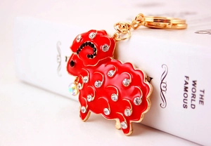 Close-up of red rhinestone sheep keychain with gold metal ring on a white book surface