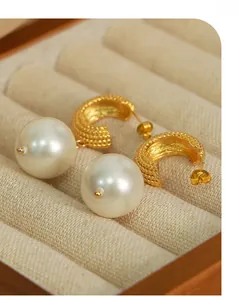 Close-up of C-shaped gold textured earrings with large round pearls on soft fabric