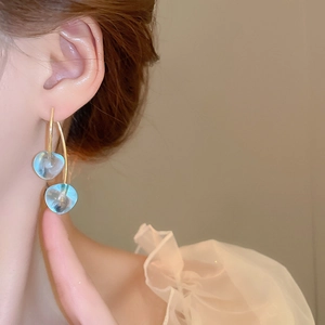 Close-up of elegant light blue resin drop earrings with gold hooks on a model