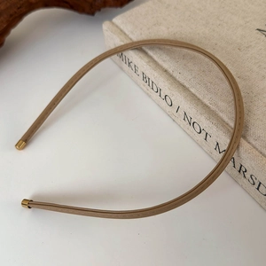 Detail of slim khaki leather headband with premium gold metal ends on a book
