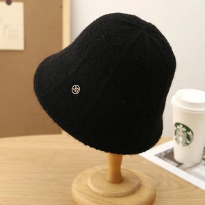 Plush black knit bucket hat with metal logo plate on a wooden display stand