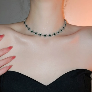 Close-up of silver flower pendant necklace with green gems and diamond accents