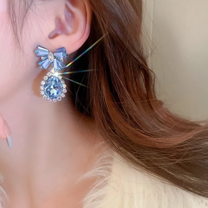 Close-up of a blue crystal bow drop earring with shimmering stones on a female model