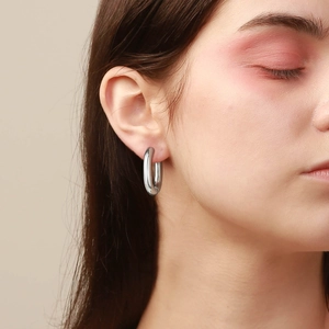 Macro side view of minimalist polished silver octagonal hoop earrings worn by a model