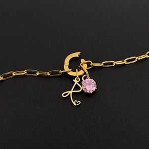 Detailopname van een gouden titanium stalen armband met roze edelsteen en de letter P