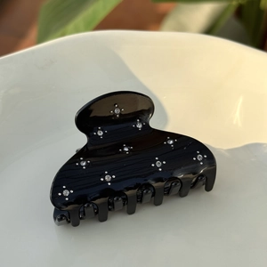 Detail of a shiny black acetate hair claw clip decorated with sparkling star rhinestones
