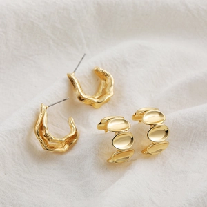 Close-up of golden geometric stud earrings with organic texture on white fabric