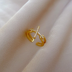 Macro detail of gold-plated cross ring with pavé-set white zircon on beige satin fabric